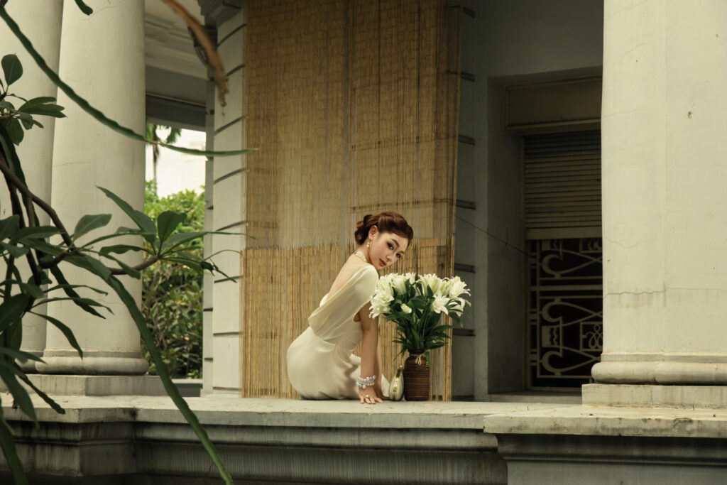 Trần Hà Linh đứng giữa không gian có cột đá và cầu thang gỗ
