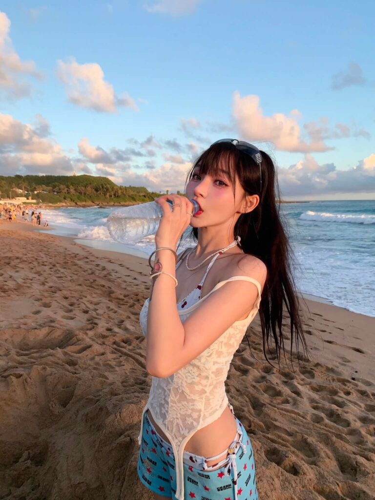 Mizuki cầm chai nước khi chụp ảnh bên bờ biển