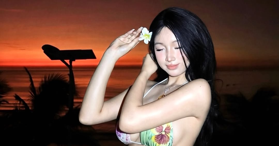 Nhi Thỏ đứng bên lan can hướng ra biển trong ánh bình minh