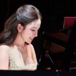 Vivi Pham diện đầm dạ hội màu kem ngồi bên cây đàn piano